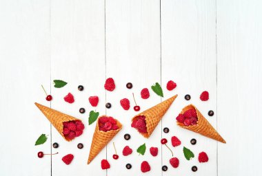 Üstten görünüm tatlı taze organik ahududu, siyah kuş üzümü ve kiraz gözleme koni boş kopya alanı ile. Taze çilek koni Beyaz ahşap zemin üzerinde. Yaz ve sağlıklı gıda kavramı, düz yatıyordu