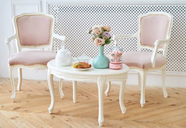 İki pembe yumuşak sandalye ve Kahvaltı ile beyaz ahşap yuvarlak masa, çiçekli vazo ve atları ile müzikal carousel atlıkarınca. Güzel modern iç, kopya alanı