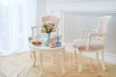 İki pembe yumuşak sandalye ve Kahvaltı ile beyaz ahşap yuvarlak masa, çiçekli vazo ve atları ile müzikal carousel atlıkarınca. Güzel modern iç, kopya alanı