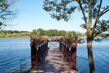 Nehir ahşap iskele tencere, açık gökyüzü ve masmavi bir deniz, kopya alanı pembe petunyaların çiçeklerle. Yaz nehir doğa manzara