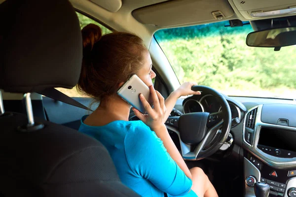 Back view of beautiful young woman driving a car and talking on smart phone, free space. Business woman sitting in car with cell phone,  looking on road