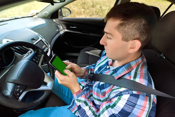 Young man driver using smart phone in car. Driver sitting in car and holding mobile smart phone with isolated screen. Modern smartphone with blank screen, copy space for text or design