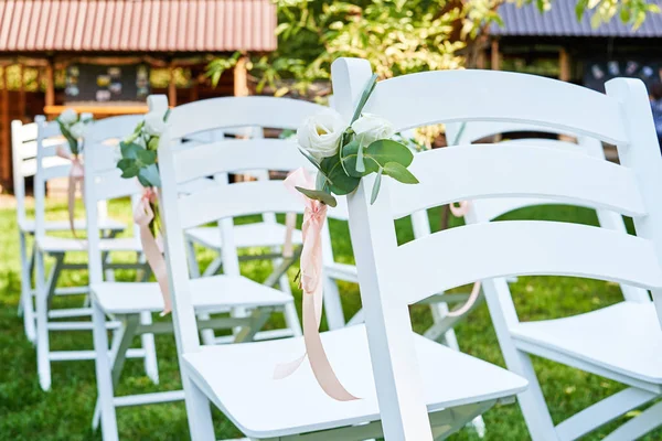 在拱门 Outroods 两侧的婚礼椅上的白色鲜花与粉红色丝带 复制空间 在花园里的草坪上为客人准备的木制椅子婚礼仪式 — 图库照片