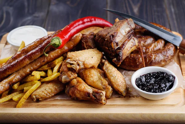 Karışık taze ızgara et ve sosis biber, patates kızartması ve ahşap kesme tahtası üzerinde sos ile. Çeşitli et yemekten yaz barbekü. sağlıklı sebze ile. Lezzetli Mangalda pirzola