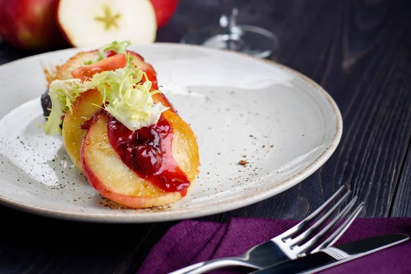 Grilled goose liver (foie gras) with sweet berry sauce and caramelized apples in white plate on table, free space. French cuisine, delicatessen restaurant meal, close up