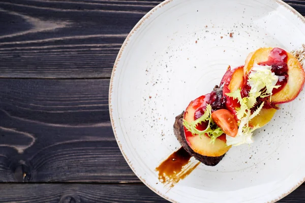 Grilled goose liver (foie gras) with sweet berry sauce and caramelized apples in white plate on table, copy space. French cuisine, delicatessen restaurant meal. Top view, flat lay