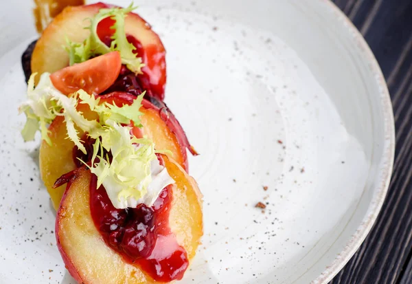 Grilled goose liver (foie gras) with sweet berry sauce and caramelized apples in white plate on table, free space. French cuisine, delicatessen restaurant meal, close up