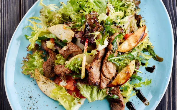 Dana salatası marul, elma, armut ve koyu ahşap arka plan, kopya alanı üzerinde mavi plaka üzerinde. Üstten görünüm, düz yatıyordu. Restoran gıda, yakın. Et salatası