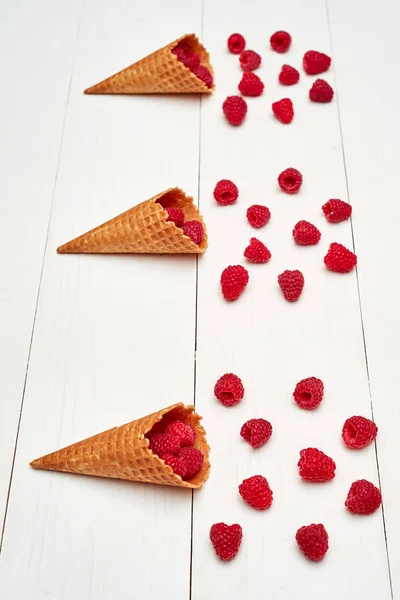 Ripe sweet raspberries in ice cream waffle cone, copy space. Fresh berries on white wooden background, free space. Summer and healthy food concept. Top view. Berries background. Raspberries explosion