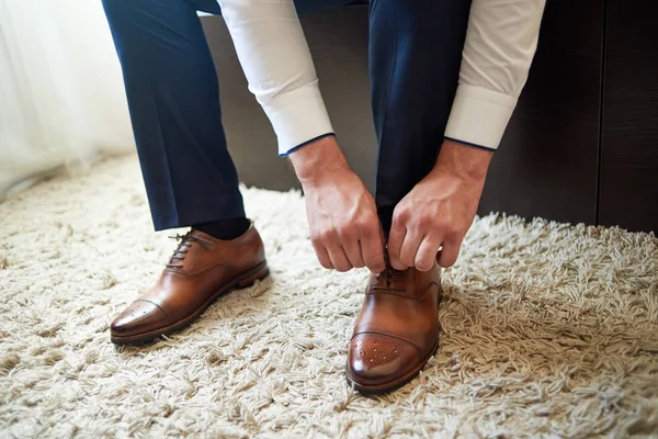 Businessman tying shoe laces indoors, close up. Man dressing up with elegant leather shoes. Groom preparing for wedding ceremony at wedding day. Man getting ready for work