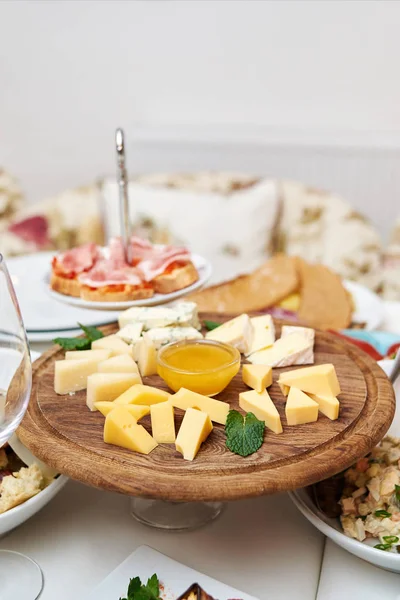 Wooden board with assortment of delicious cheese and honey on dinner table. Various types of cheese. Cheese plate with Dorblu, Parmesan, Brie, Camembert and Roquefort. Cheese Platter
