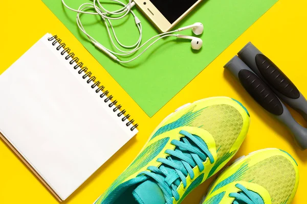 Sports equipment with shoes, skipping rope, blank notebook and mobile cellphone with earphones on colorful background. Top view, flat lay. Sport, fitness concept, healthy lifestyle