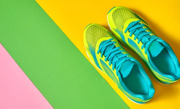 Pair of sport shoes on colorful background. New sneakers on green, yellow and pink background, copy space. Overhead shot of running shoes. Top view, flat lay