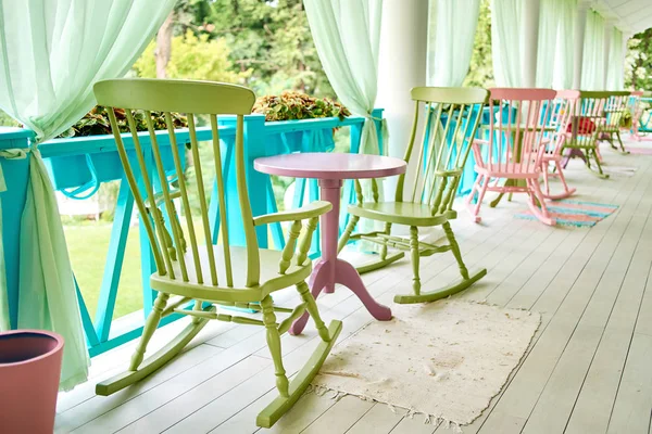 Pink and green wooden rocking chairs and table on porch or balcony. Two relaxing armchairs on porch of luxury hotel. Empty cafe with rocking chairs and table on summer  terrace outdoor, copy space