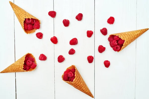 Ripe sweet raspberries in ice cream waffle cone, copy space. Fresh berries on white wooden background, free space. Summer and healthy food concept. Top view, flat lay. Berries background