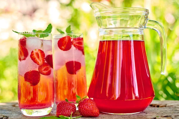 Çilek limonata, buz ve gözlük ve sürahi ile yeşil arka plan açık havada, nane ile kokteyl alanı kopyalayın. Canlandırıcı yaz berry içeceği. Köpüklü içecek gözlük 