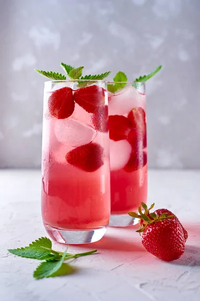 Strawberry lemonade, cocktail with ice and mint in glass on gray stone concrete table background, copy space. Refreshing summer berry drink. Sparkling drink in glasses with slices of strawberry