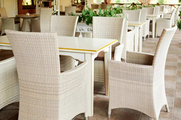 Empty cafe with rattan wicker armchairs and tables on summer garden terrace outdoor, free space. Table and chairs in empty cafe. Wicker furniture rattan chairs on terrace
