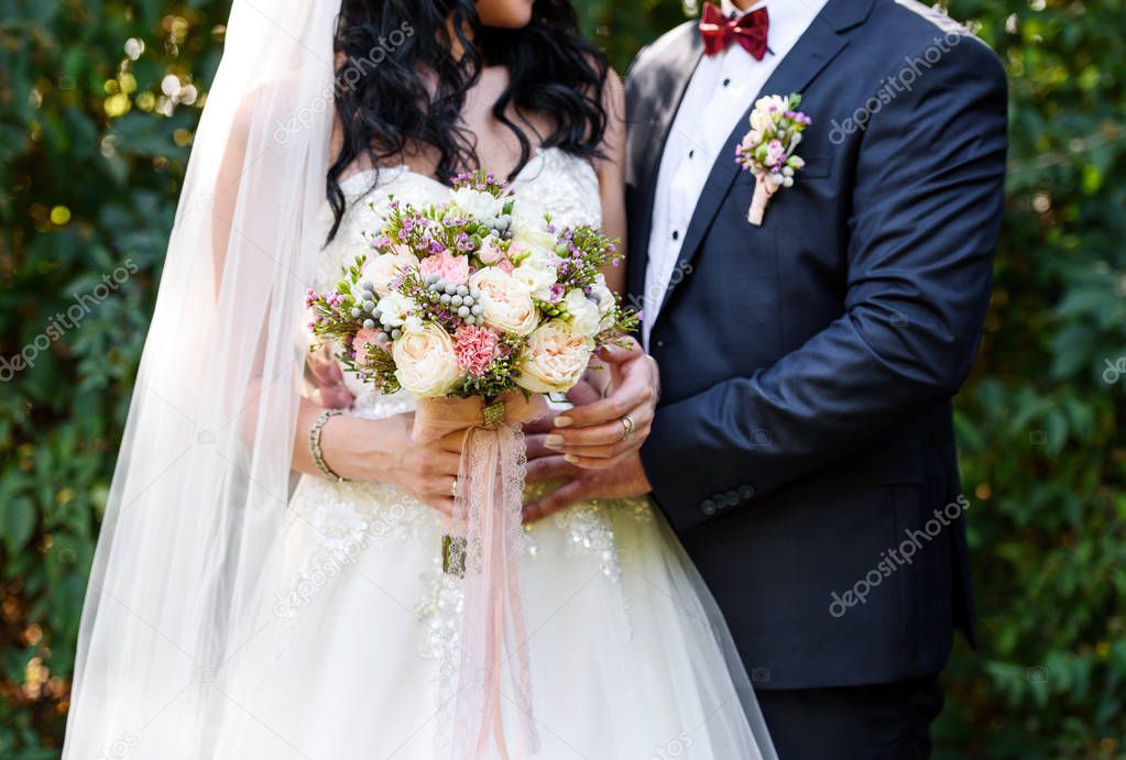 Beautiful lush bridal bouquet with lace ribbons in bride's hand. Happy bride and groom hugging after wedding ceremony, free space. Wedding couple, newlyweds, free space