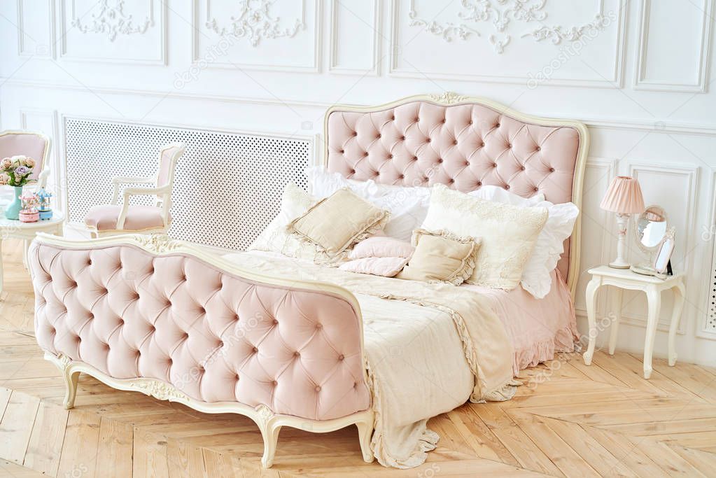 Big royal bed with pillows in elegant bedroom interior, copy space. Honeymoon suite, free space. Female bedroom in pink and white colors. Luxury bed in romantic style bedroom in white room. Boudoir