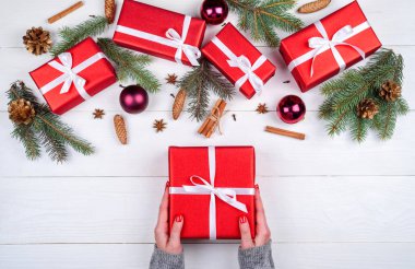 Eller kırmızı Noel hediye kutusunda Noel süsleri (hediye, çam ağacı, çam kozalakları, tarçın ve Yıldız anason), Beyaz ahşap zemin üzerine kopya alanı tutan kadın. Düz yatıyordu, en iyi görünümü 