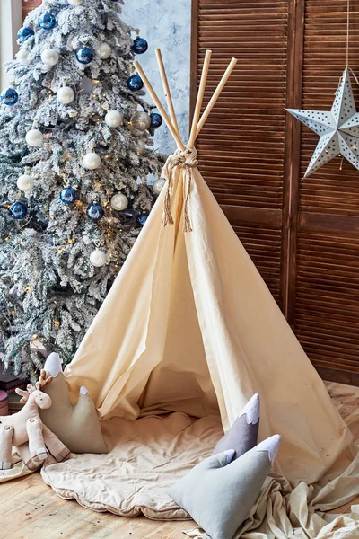 Christmas tree with gifts and wigwam in child room, copy space. Christmas decorations. Childen room interior with decorated play tipi tent. Scandinavian style
