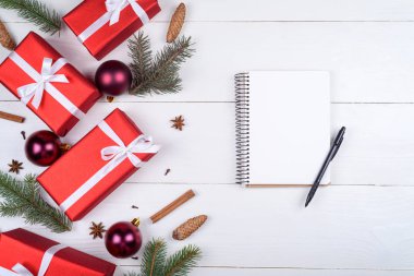 Beyaz ahşap arka planda xmas süslemeleri, kopya alanı ile üstten görünüm boş defter. Defter için istek listesi veya yapılacaklar listesi, kırmızı hediye kutuları, köknar ağacı dalları ile Noel arka plan. Düz yatıyordu