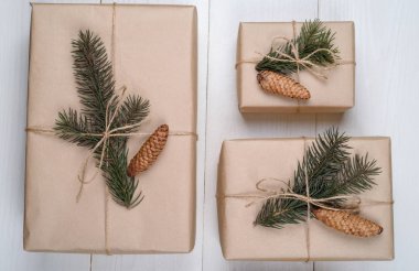 Noel arka plan hediye kutuları ile kraft kağıt köknar ağaç dalları ve beyaz ahşap arka planda, boş alan koni ile sarılı. Tatil tebrik kartı, kopya alanı. Düz yatıyordu, en iyi görünümü 