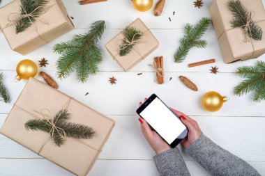 Eller ile mobil akıllı telefon ile app sunuda, kopya alanı boş perde. Noel hediyeleri kraft ahşap arka plan üzerinde sarılı. Düz yatıyordu, en iyi görünüm. Uygulama şablonu sahte 