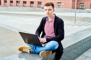 Açık havada üniversite kampüsü içinde oturan ve laptop ile çalışma, sınavlara hazırlık, yazarak, internet'te sörf, dinlenme, kopya alanı öğrenci. Teknoloji, eğitim kavramı