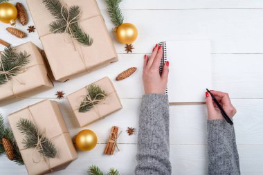 Üstten görünüm kadın el ile gol yazma kalemi veya Noel hediye boxex ahşap zemin, boş alan üzerine yakınındaki boş defter listelemek için. Düz yatıyordu. Tatil hediye kutuları kraft içinde sarılmış