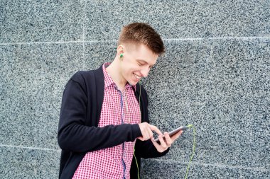 Taş duvara yakın duran ve cep telefonu kulaklık ile müzik dinlemek, yazarak, internet'te sörf, geri kalan üniversite kampüs mekanlarda, kopya alanı olan gülümseyen öğrenci. Eğitim, dinlenmek ve rahatlamak kavramı