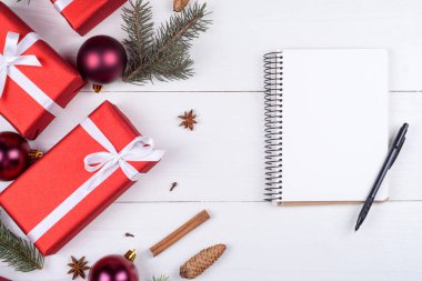 Beyaz ahşap arka planda xmas süslemeleri, kopya alanı ile üstten görünüm boş defter. Defter için istek listesi veya yapılacaklar listesi, kırmızı hediye kutuları, köknar ağacı dalları ile Noel arka plan. Düz yatıyordu