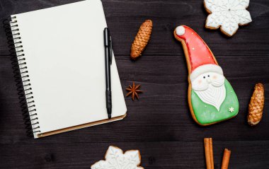 Açık boş defter ile kopya alanı metin ve koyu ahşap masa üzerinde ev yapımı gingerbread çerezleri için. Üstten görünüm, düz yatıyordu. Noel arka plan. Noel Baba, boş alan için istek listesi