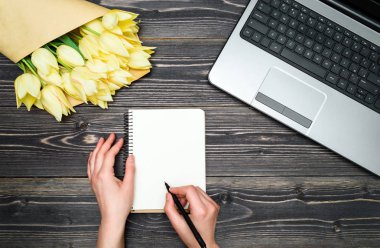 Defter ile yazma kadın eller iş dizüstü bilgisayar ve buket sarı laleler, kopya alanı açın. Bayan günü, Mart 8, anneler günü, Paskalya. İş kavramı. Düz yatıyordu, en iyi görünümü
