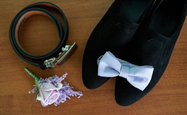Siyah süet erkek ayakkabı, mavi kravat, kemer ve mor yaka çiçeği ahşap arka plan üzerinde yakın çekim. Modern damat aksesuarları. Düğün detayları. Erkek casual kıyafetler. Üstten görünüm, düz yatıyordu