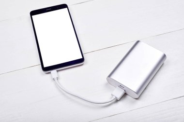 Beyaz ahşap Resepsiyon arka planda, boş alan güç banka (pil banka) ile şarj beyaz boş ekran ile mobil akıllı telefon. Üstten görünüm kopya alanı ile. Teknoloji kavramı