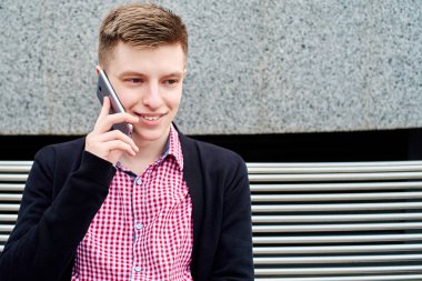Üniversite Kampüsü, kopya alanı içinde kalan sahip tek başına bankta oturan ve cep telefonu üzerinde konuşurken erkek öğrenci portresi. Eğitim, dinlenmek ve rahatlamak, seyahat ve Turizm kavramı