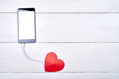 Mobil akıllı telefon ile kopya alanı beyaz ahşap arka plan üzerinde kırmızı kağıt kalp ile şarj beyaz boş perde. Sevgililer günü için mockup şablonu. Aşk, teknoloji kavramı. Üstten görünüm, düz yatıyordu