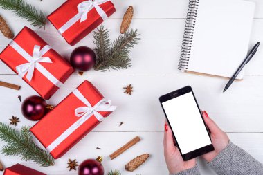 Noel hediye kutuları, baubles, dalları, ahşap arka plan üstünde boş defter ile arka plan. Mobil akıllı telefon, holding kadın eller kapatın. App sunuda, kopya alanı boş dokunmatik ekran