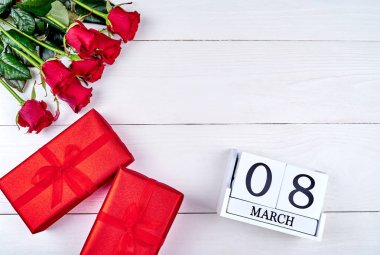 Kırmızı hediye kutuları, güller ve beyaz ahşap arka planda, küp takvim metin için yer kopyalayın. Tarihi beyaz blok takvim 8 Mart kadın günler için sakla. Tebrik kartı. Üstten görünüm, düz yatıyordu