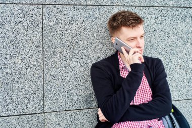 Üniversite Kampüsü, kopya alanı içinde kalan sahip gri taş duvara yakın tek başına duran ve cep telefonu üzerinde konuşurken erkek öğrenci portresi. Eğitim, dinlenmek ve rahatlamak, seyahat ve Turizm kavramı