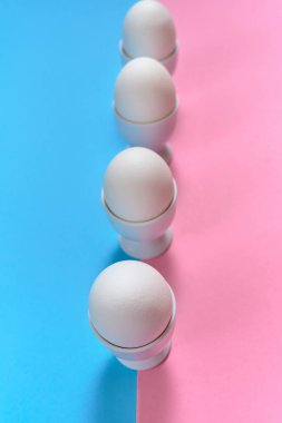 Beyaz yumurta yumurtalık mavi ve pembe pastel arka plan, kopya alanı üzerinde tutuyoruz. Satır standında iki tonu renk kağıt zemin üzerine haşlanmış yumurta. Sağlıklı gıda kavramı. Paskalya yumurtaları. Üstten görünüm
