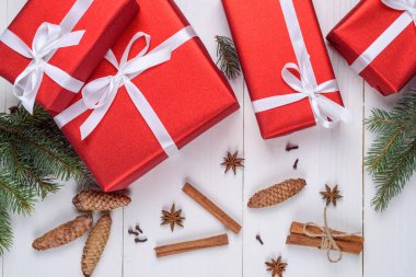 Noel arka plan kırmızı hediye kutuları, köknar ağacı dalları, çam kozalakları, tarçın ile sopa ve anason yıldız. Beyaz ahşap zemin üzerinde kırmızı Noel hediye kutuları. Tatil tebrik kartı. Düz yatıyordu üstten görünüm 