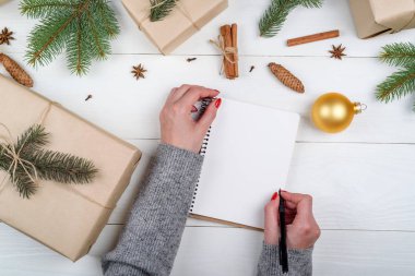 Üstten görünüm kadın el ile gol yazma kalemi veya Noel hediye boxex ahşap zemin, boş alan üzerine yakınındaki boş defter listelemek için. Düz yatıyordu. Tatil hediye kutuları kraft içinde sarılmış