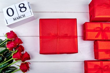 Kırmızı hediye kutuları, güller ve beyaz ahşap arka planda, küp takvim metin için yer kopyalayın. Tarihi beyaz blok takvim 8 Mart kadın günler için sakla. Tebrik kartı. Üstten görünüm, düz yatıyordu