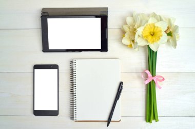 Nergis (narcissus), tablet ve cellphone boş ekran ve ahşap zemin, kopya alanı üzerine boş defter ile buket. Üstten görünüm, düz yatıyordu. Bahar çiçekleri. Bayan günü, anneler günü, Paskalya