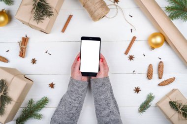 Mobil akıllı telefon ile app sununun süslemeleri, kopya alanı ile kadın elinde boş perde. Ahşap arka plan üzerinde Noel hediyeleri. Düz yatıyordu, en iyi görünüm. Noel uygulama şablonu sahte 