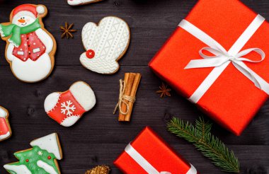 Noel zencefilli kurabiye, kırmızı hediye kutuları, köknar ağacı dalları, koyu ahşap zemin, üzerine tarçın alanı kopyalayın. Üstten görünüm, düz yatıyordu. Mitten, çam ağacı, kardan adam, çorap. Tatil kavramı