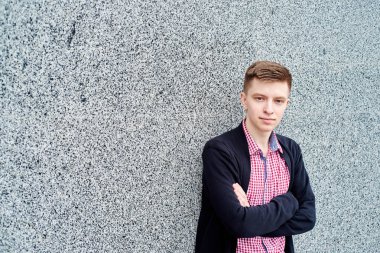 Gri taş duvar ve dinlenme açık havada, üniversite kampüsü içinde olan yakın çapraz ellerle kopya alanı ayakta yakışıklı erkek öğrenci portresi. Eğitim, dinlenmek ve rahatlamak, seyahat ve Turizm kavramı 